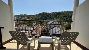 A balcony with two white plastic chairs and a small table, overlooking a residential area with houses and greenery. - Kata Place Hotel (Karon)