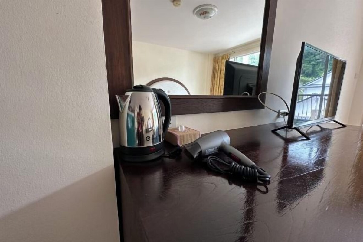 A hotel room with a wooden table, a kettle, a hairdryer, and a chair.