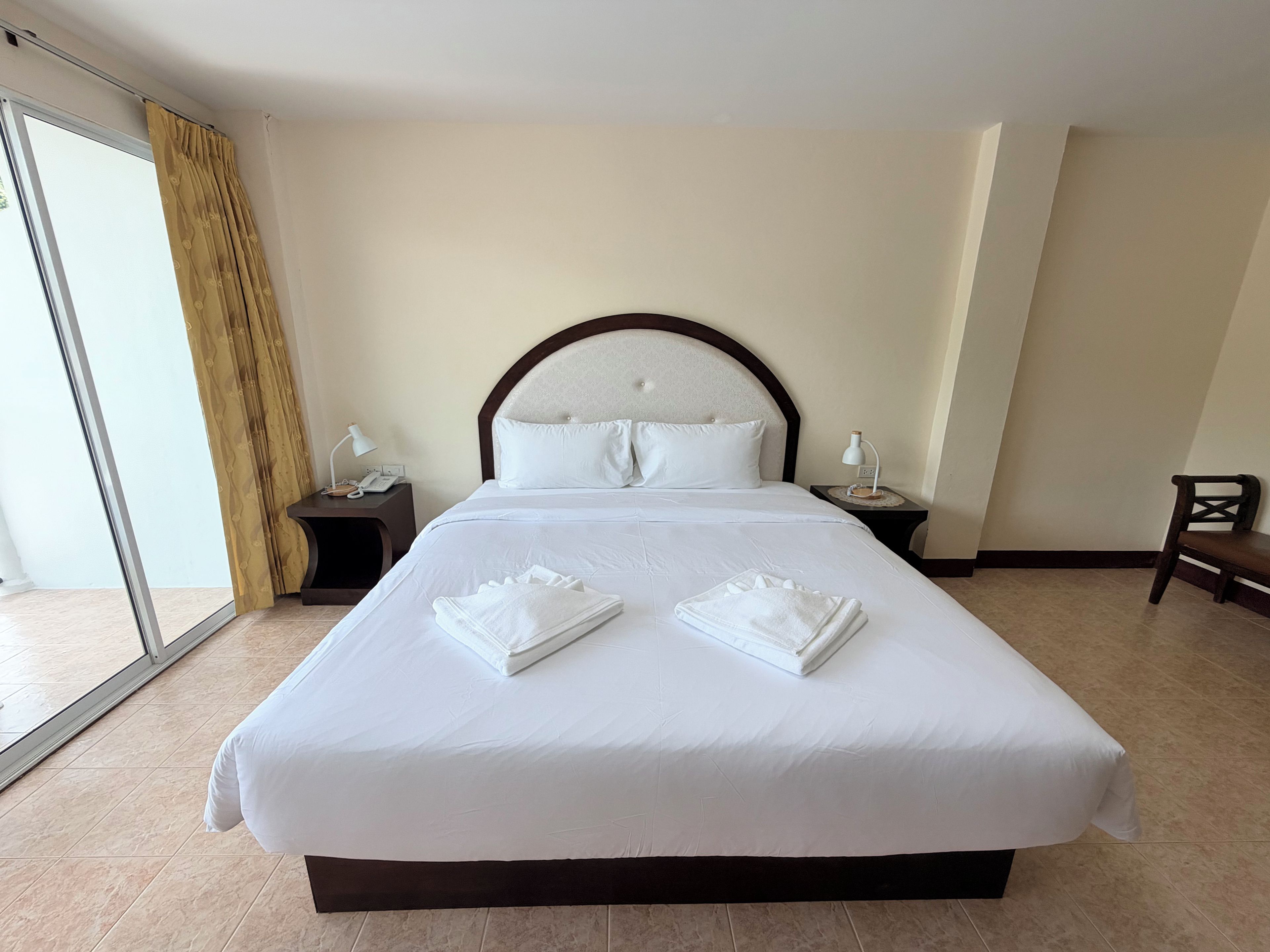 A hotel room with a large bed, two bedside tables, a chair, and a sliding glass door.