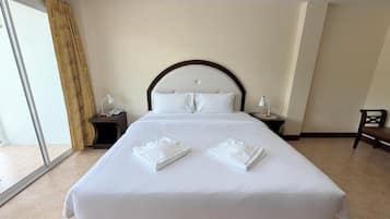 A hotel room with a large bed, two bedside tables, a chair, and a sliding glass door.
