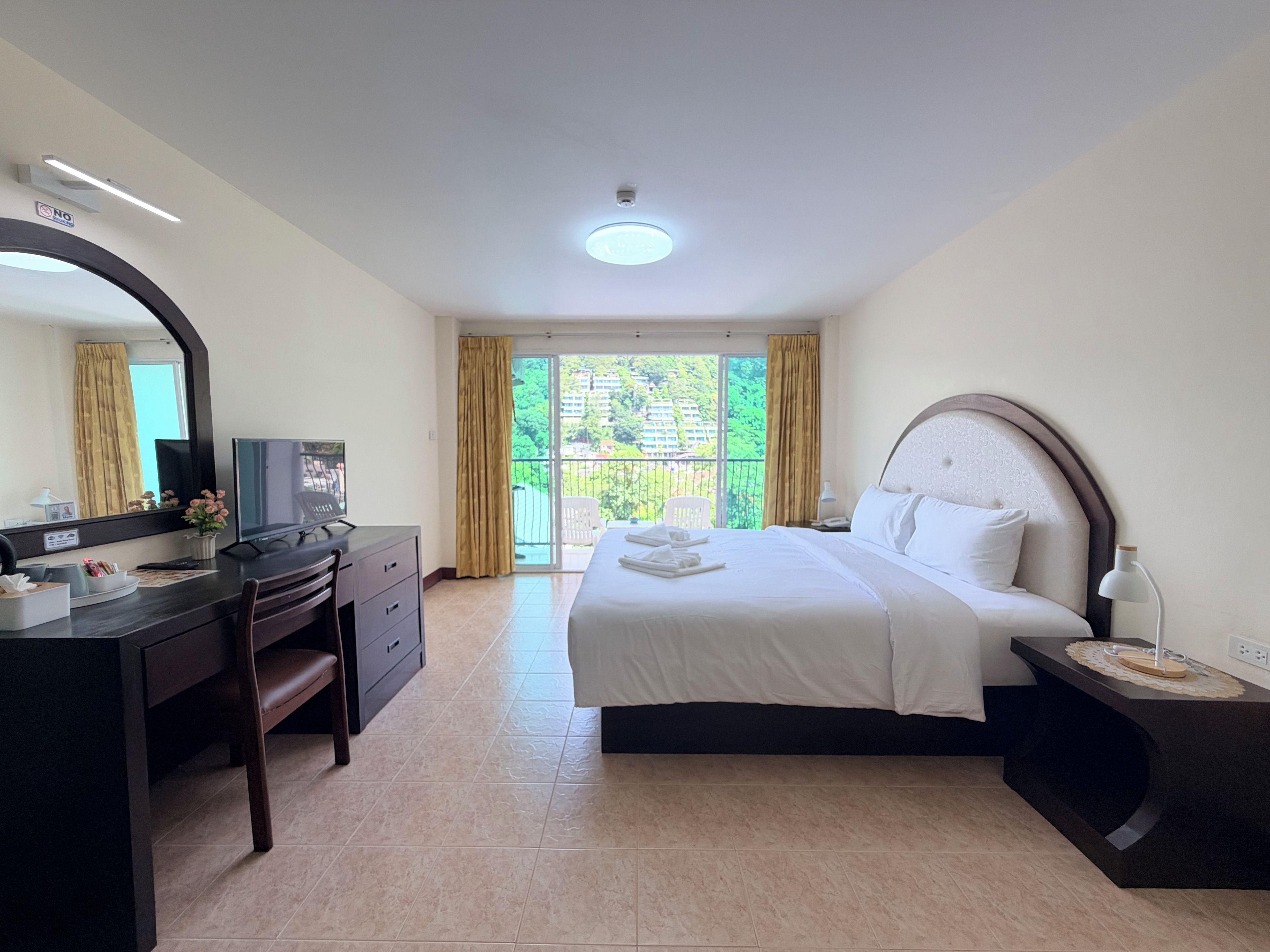 A hotel room with a bed, a desk, a television, and a balcony with curtains.