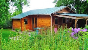 A wooden cabin with a porch, surrounded by lush greenery and flowering plants. - Les Gîtes de Petrocoriis (Boulazac-Isle-Manoire)