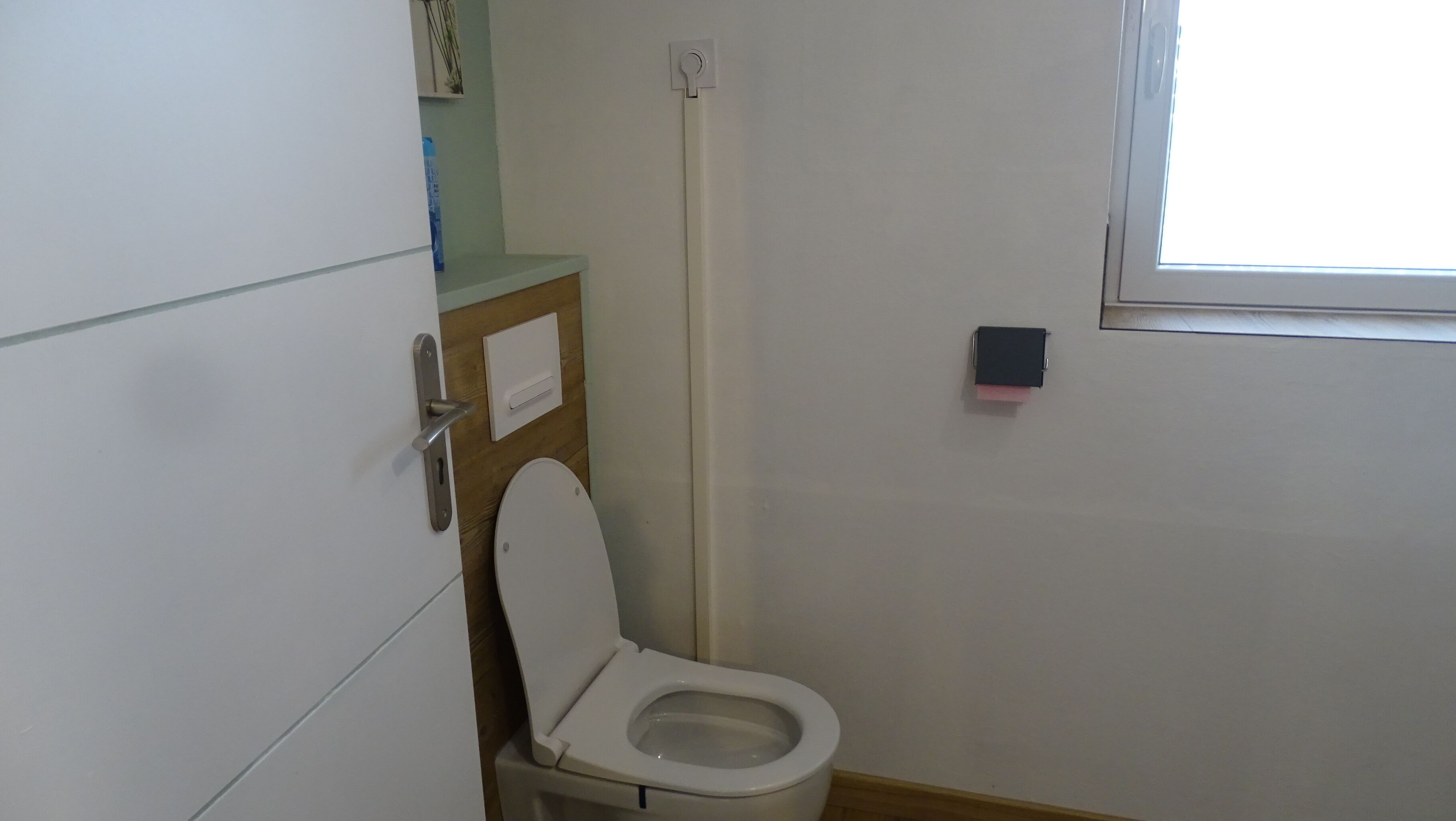 Un baño pequeño y funcional con inodoro, un armario de madera y una ventana.