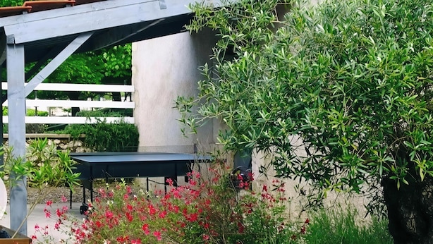 A garden area with a table under a pergola, surrounded by green foliage and red flowers. - Les Gîtes de Petrocoriis (Boulazac-Isle-Manoire)