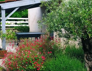 A garden area with a table under a pergola, surrounded by green foliage and red flowers. - Les Gîtes de Petrocoriis (Boulazac-Isle-Manoire)