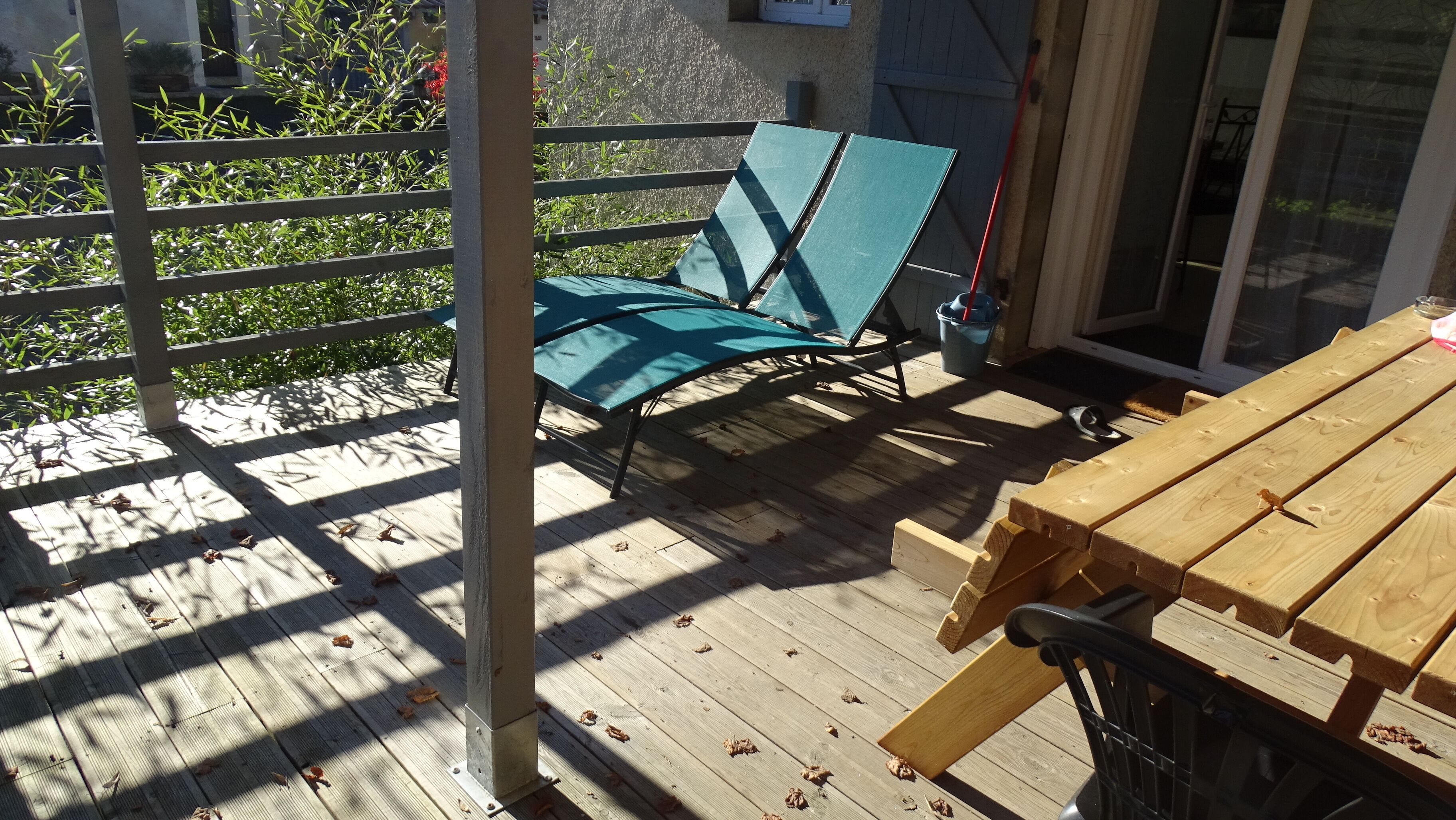 Une terrasse en bois avec une table et des chaises, une clôture en métal et une porte donnant sur un espace abrité.