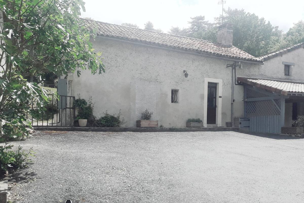 Une maison de campagne avec une allée en gravier, un petit porche et un jardin agrémenté de plantes en pot.