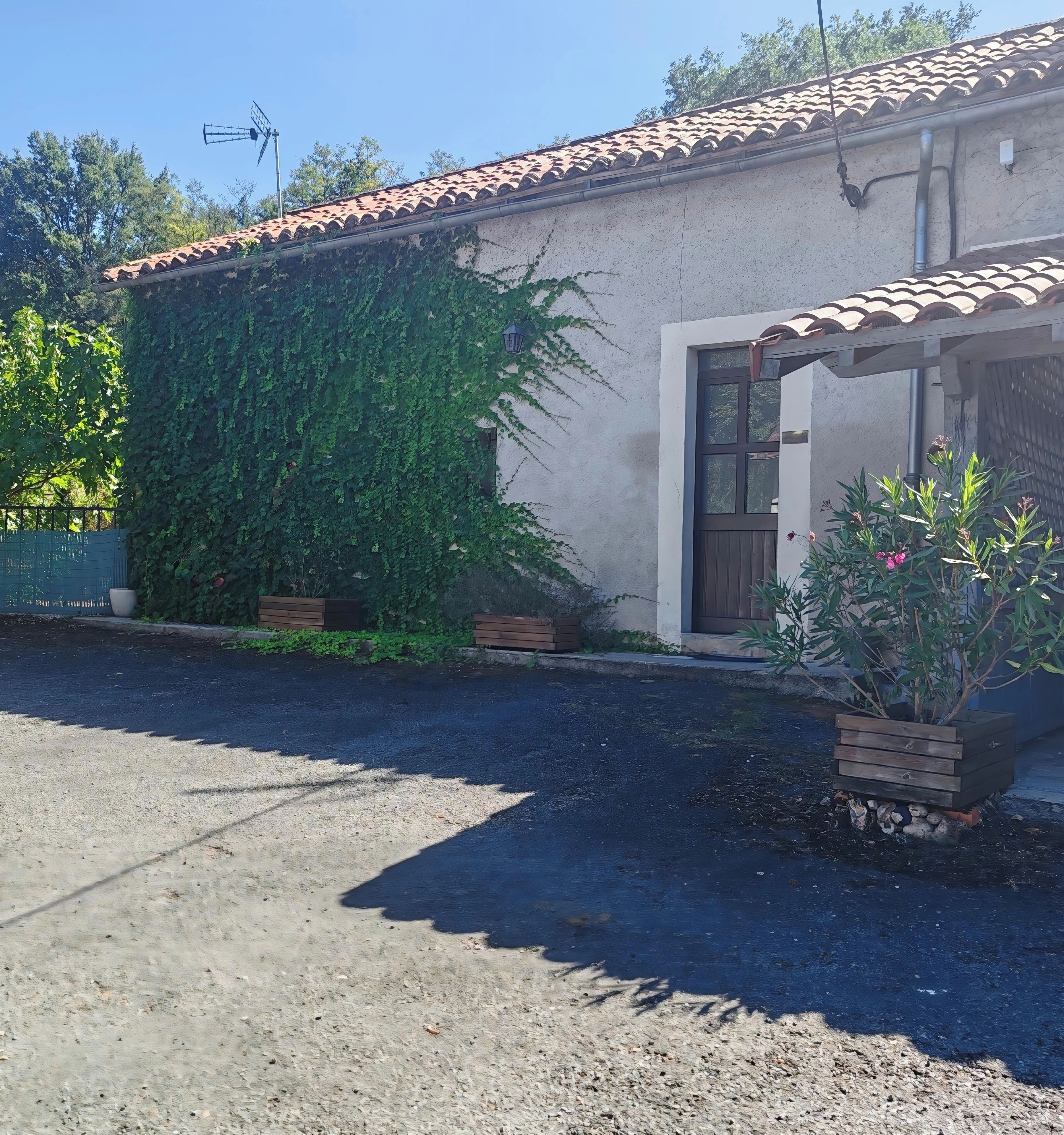 Une maison avec un toit en tuiles, une porte et une fenêtre. Il y a un jardin avec des plantes et un banc en bois.
