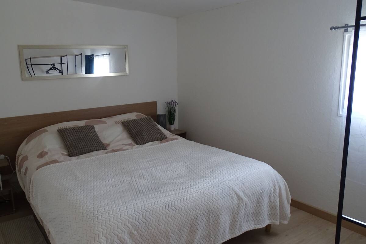 Une chambre à coucher comprenant un lit, une table de chevet, une étagère fixée au mur et une fenêtre.