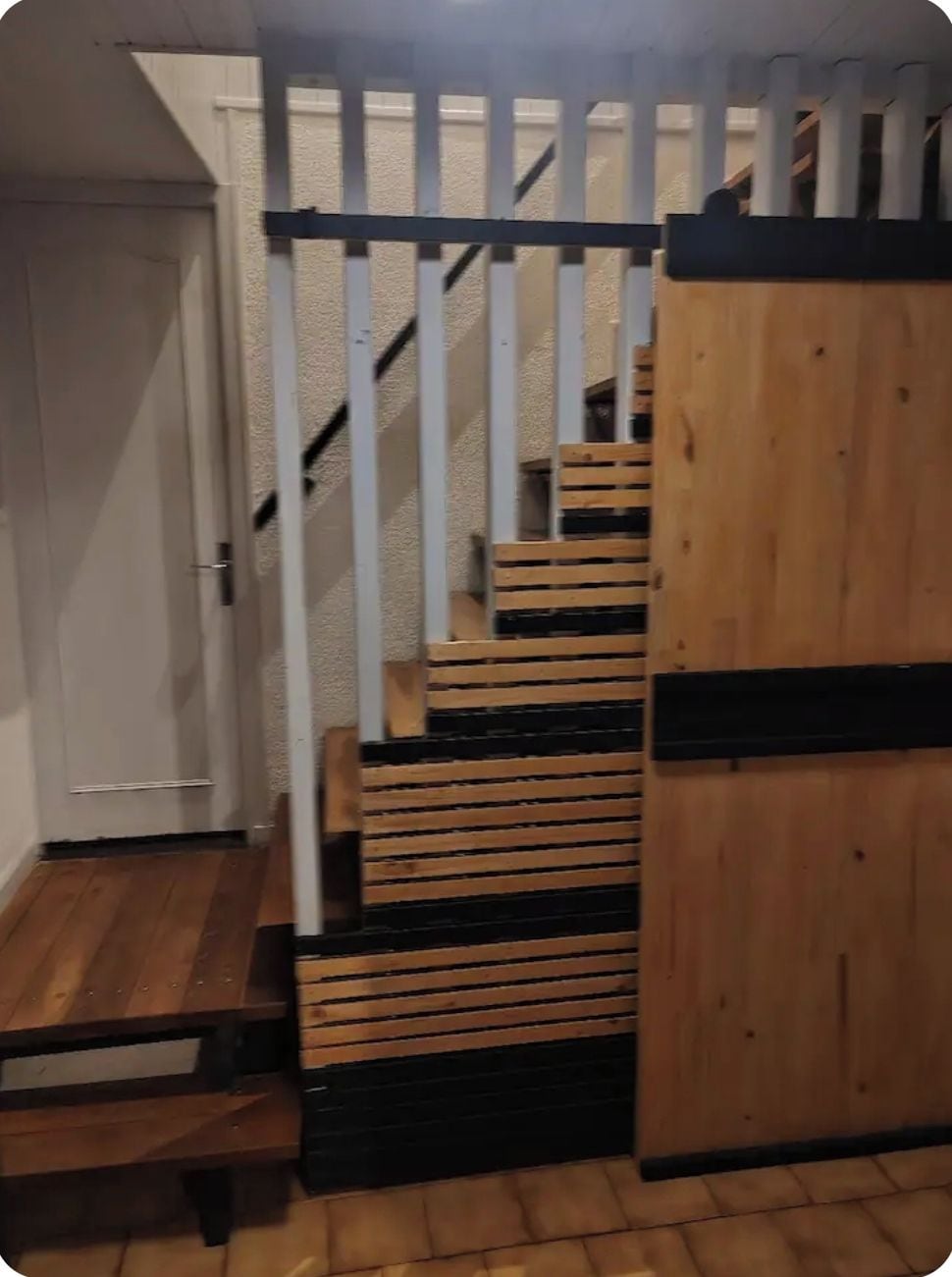 Una escalera de madera con barandilla negra y una puerta a la derecha.