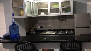 A kitchen with white cabinets, a black countertop, a sink, a stove, and two black chairs.
