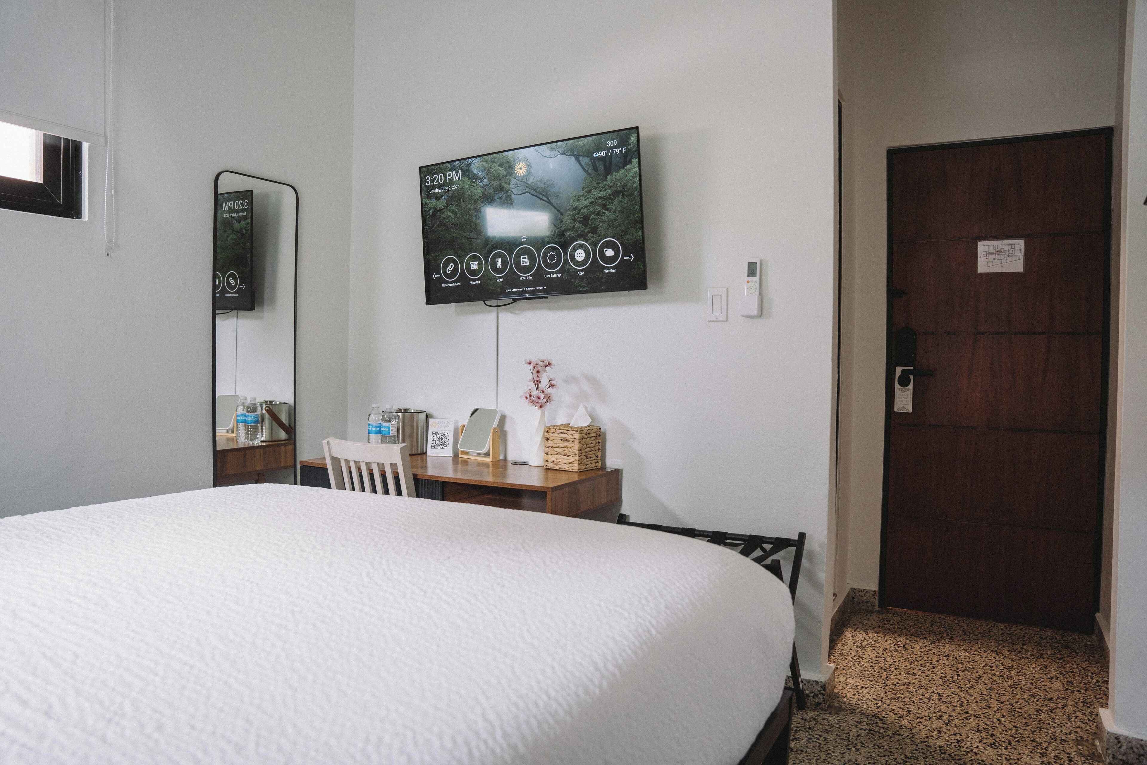 A hotel room with a large bed, a TV mounted on the wall, a desk with a chair, and a wooden door.