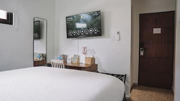 A hotel room with a large bed, a TV mounted on the wall, a desk with a chair, and a wooden door.