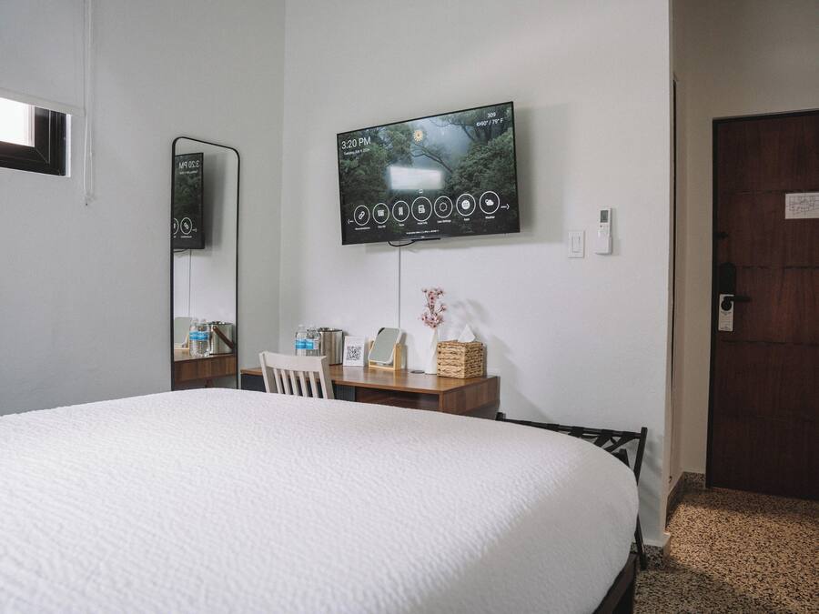 A hotel room with a large bed, a TV mounted on the wall, a desk with a chair, and a wooden door.