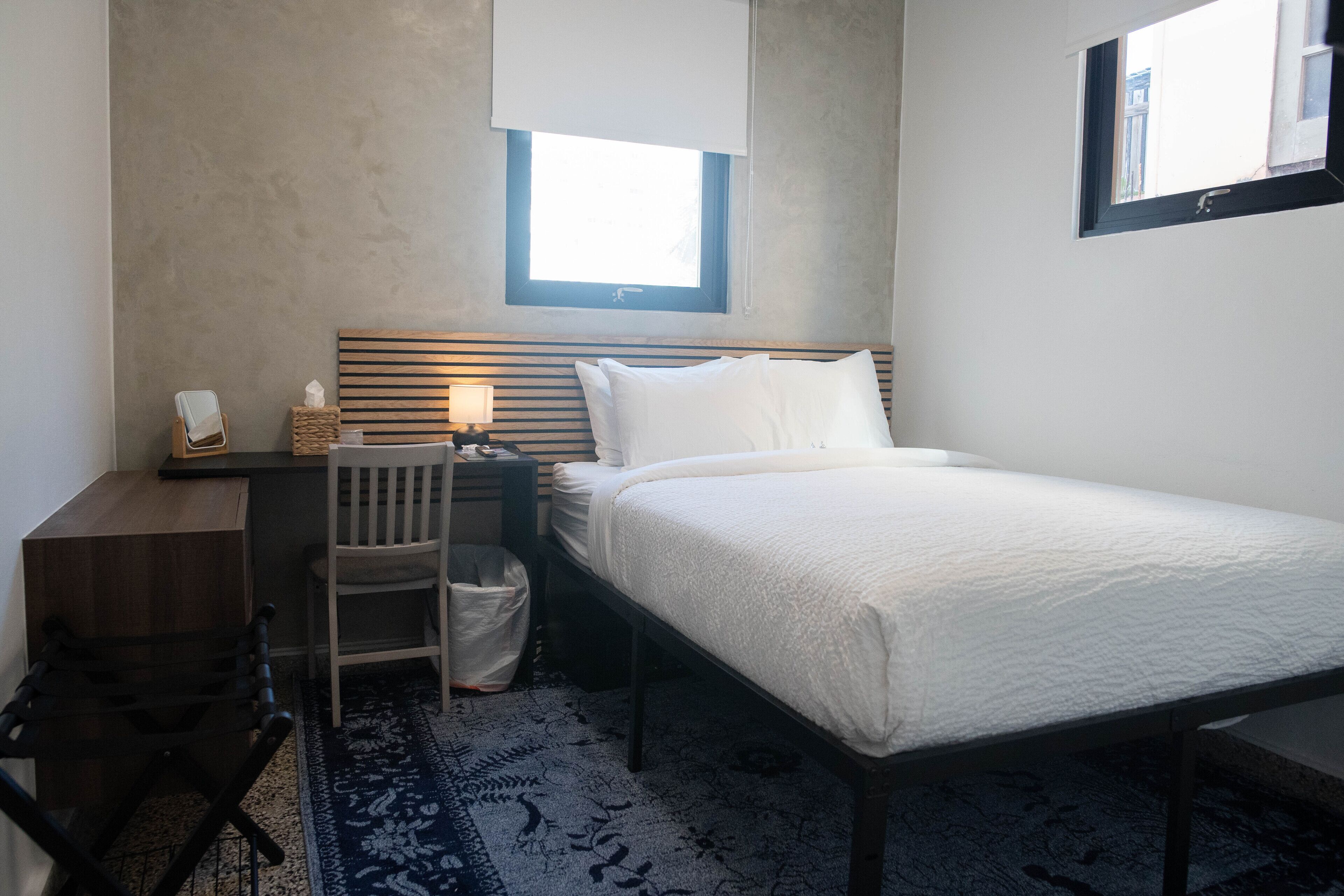 Une petite chambre à coucher, bien rangée, avec un lit, un bureau, une chaise et une fenêtre.