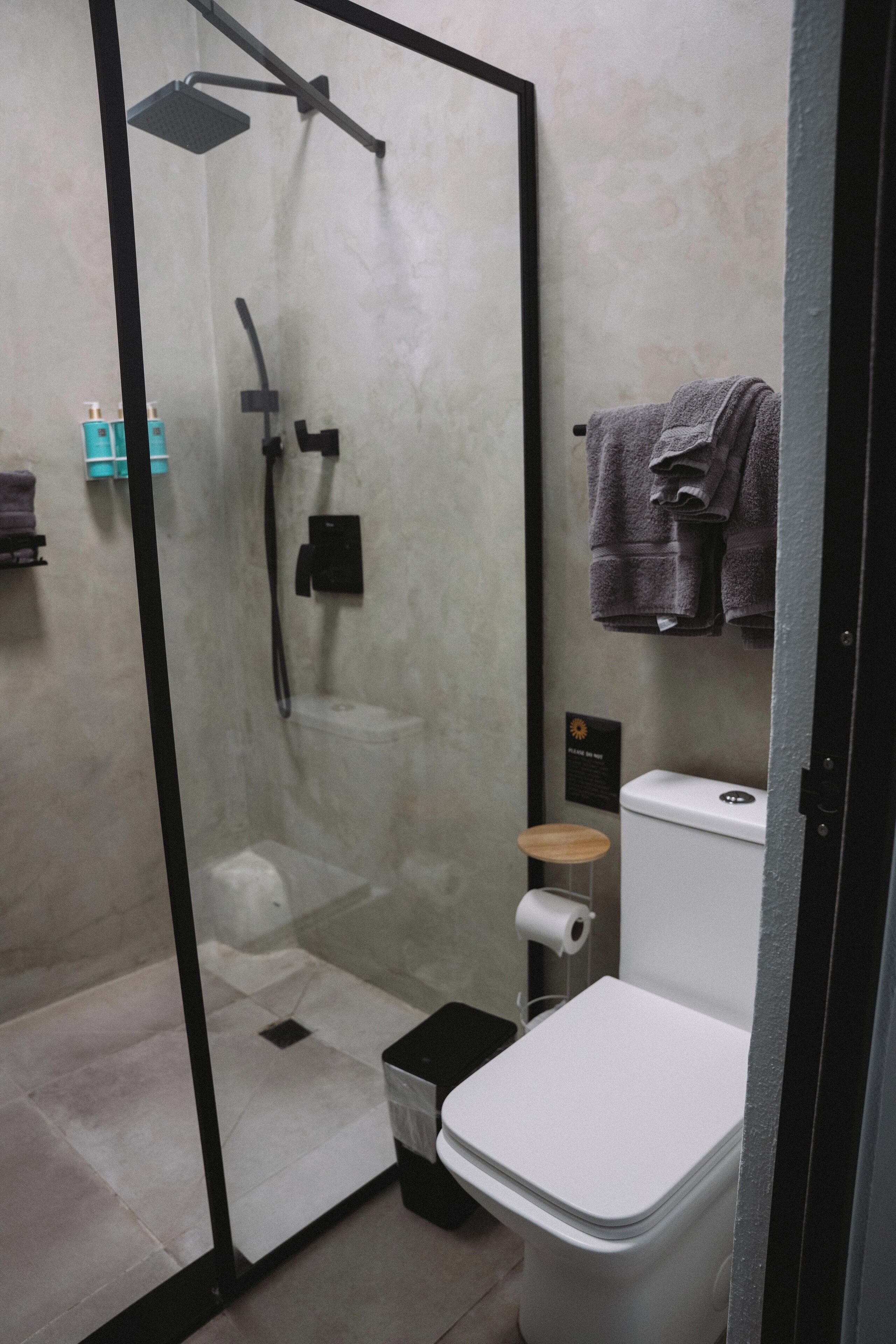 A modern bathroom with a glass-enclosed shower, a toilet, and a small wooden stool.