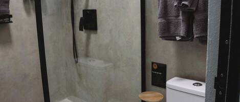 A modern bathroom with a glass-enclosed shower, a toilet, and a small wooden stool.