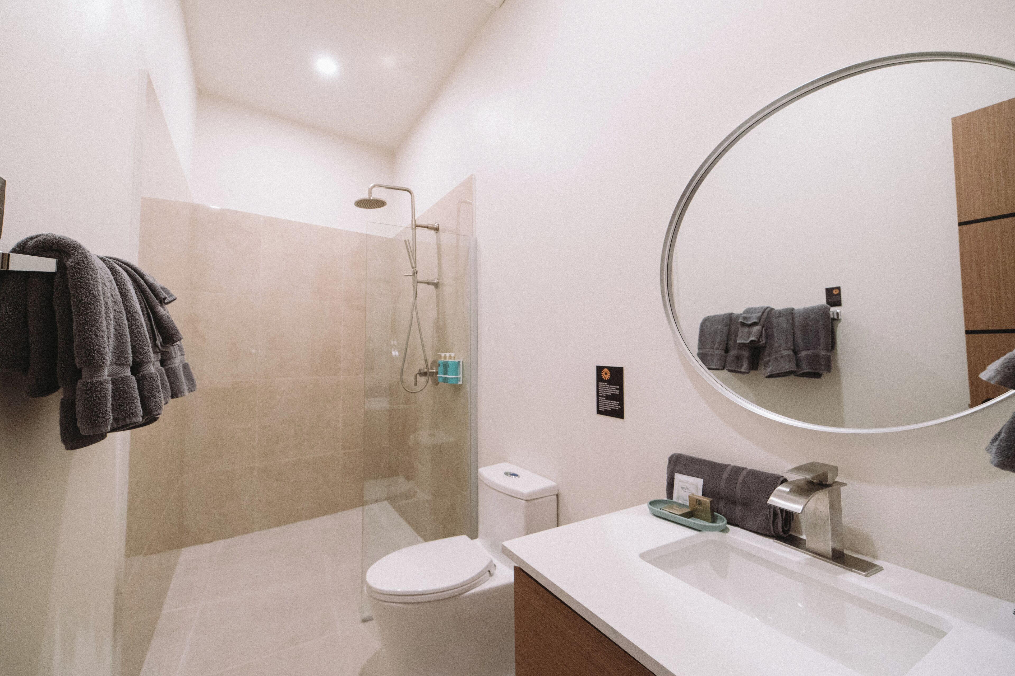 Une salle de bain moderne avec une douche à parois de verre, des toilettes blanches, un grand miroir et un lavabo blanc.