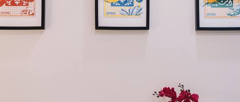 A desk with a chair, a vase with flowers, and framed artwork on the wall.