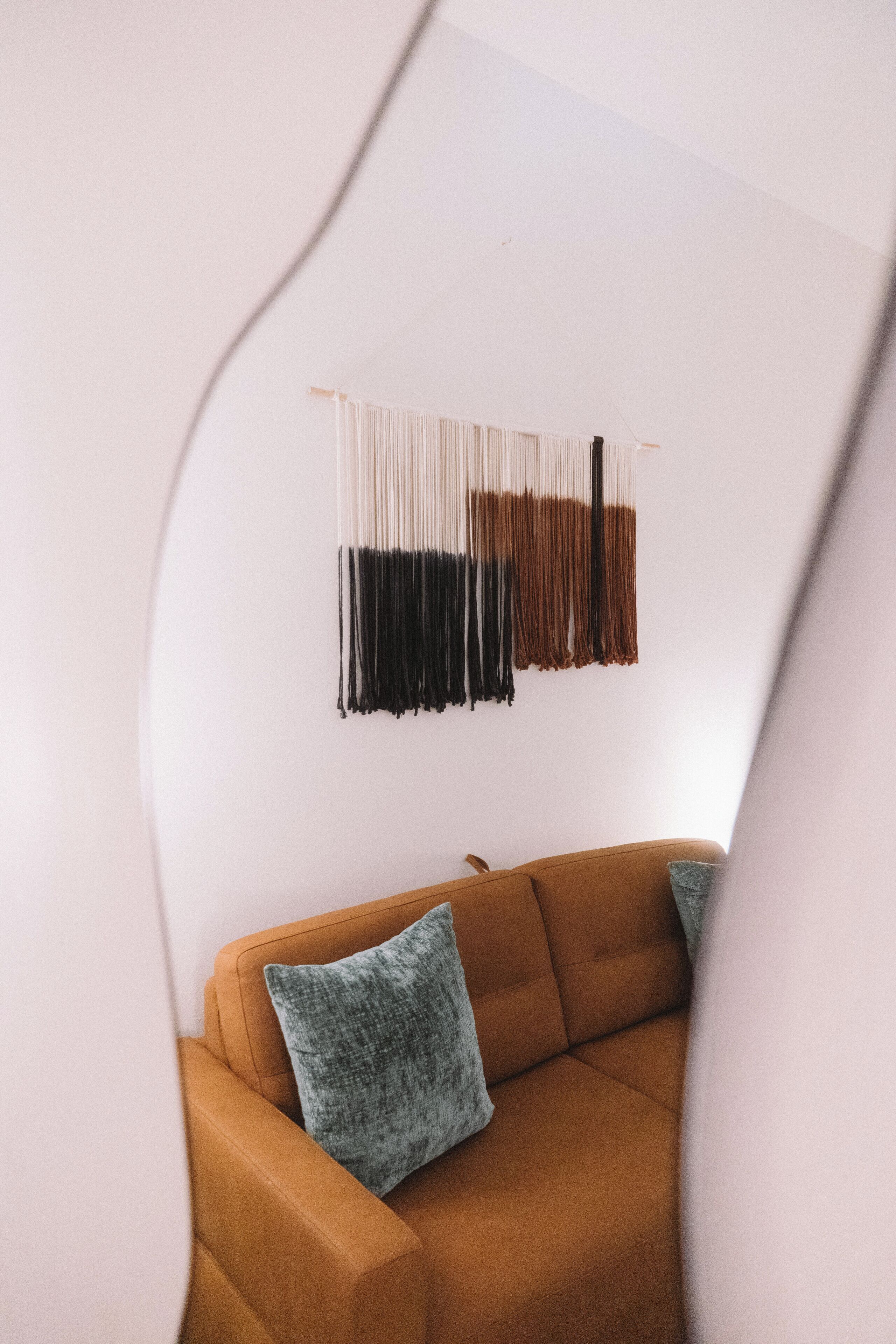 A modern living room with a brown sofa and a wall-mounted macrame piece.