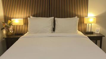 Una cama bien hecha con ropa blanca, dos mesitas de noche con lámparas y una pared con listones de madera verticales.
