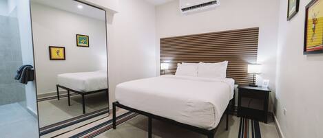 A modern hotel room with a large bed, bedside tables, a mirror, and a wall-mounted air conditioner.