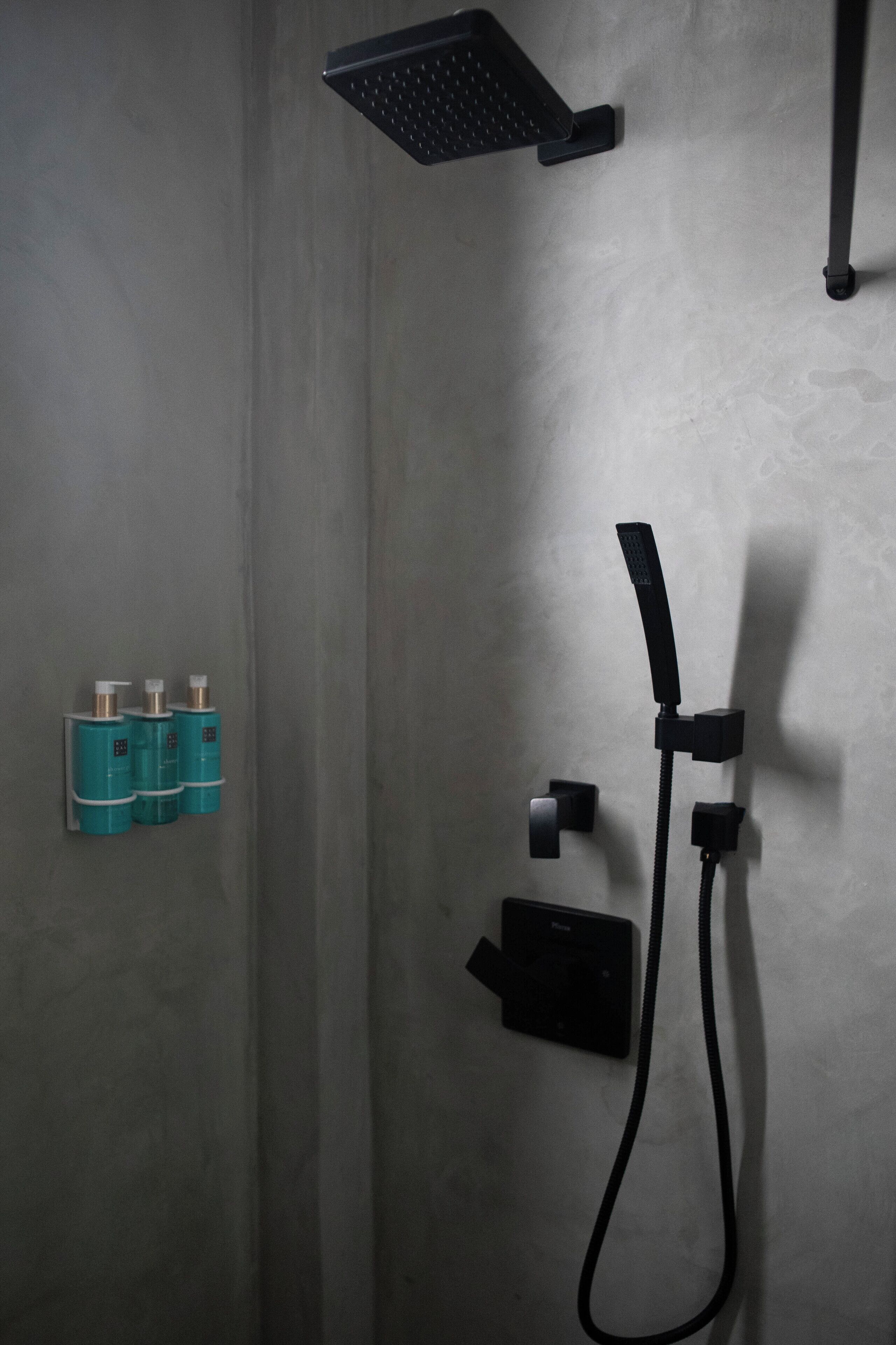A shower area with a handheld showerhead, a wall-mounted control panel, and two wall-mounted soap dispensers.