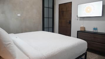 A bedroom with a bed, a wooden door, a TV on the wall, and a small dresser.