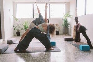 A yoga class in a room with large windows, potted plants, and exercise mats. - The Looking Glass Hotel (San Juan)