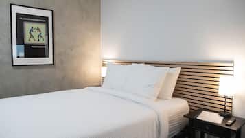 A neatly made bed with white linens, a framed picture on the wall, and a bedside table with a lamp and remote control.