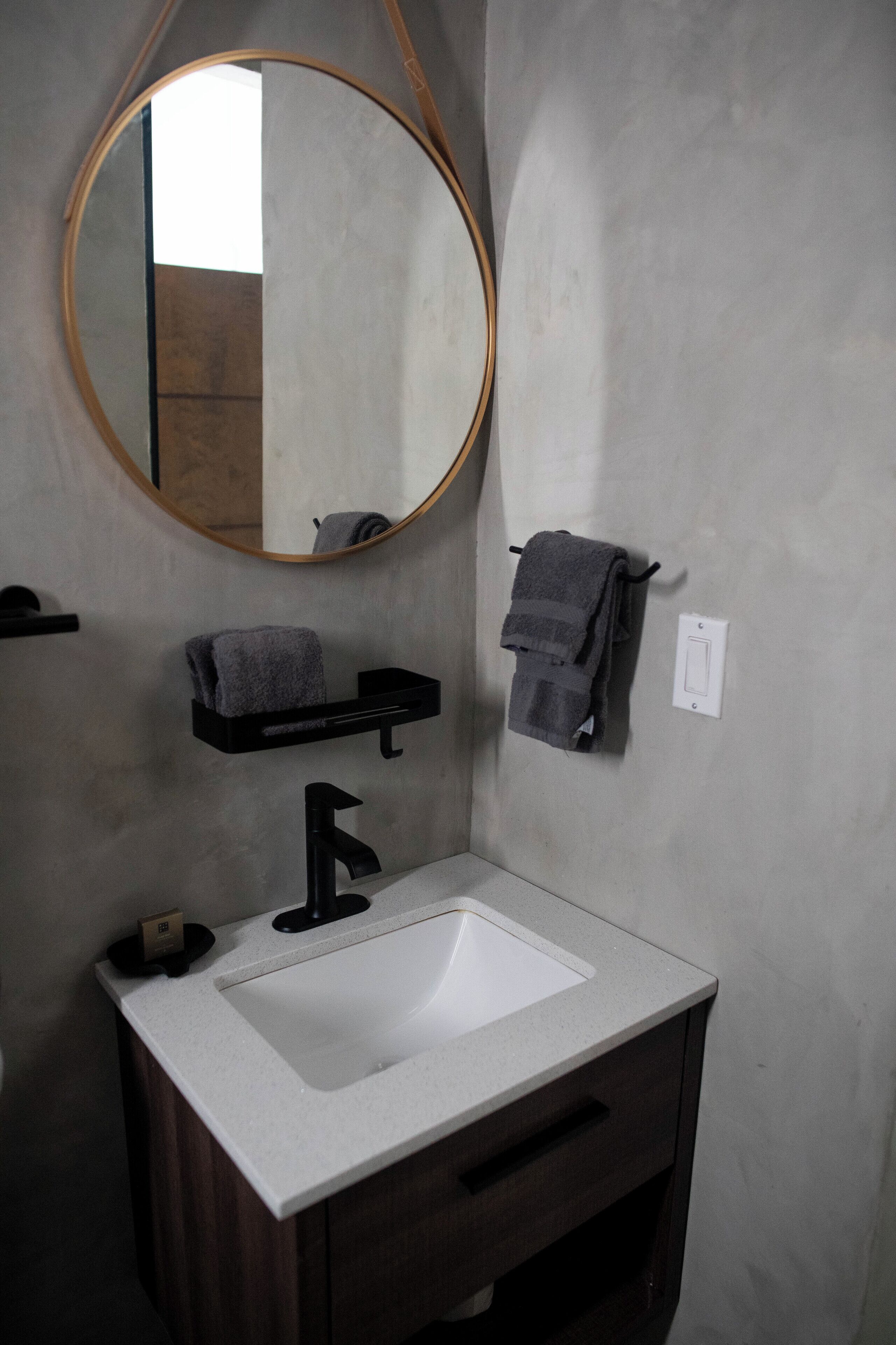 A bathroom with a white sink, dark wooden vanity, a round mirror, and two towel racks.