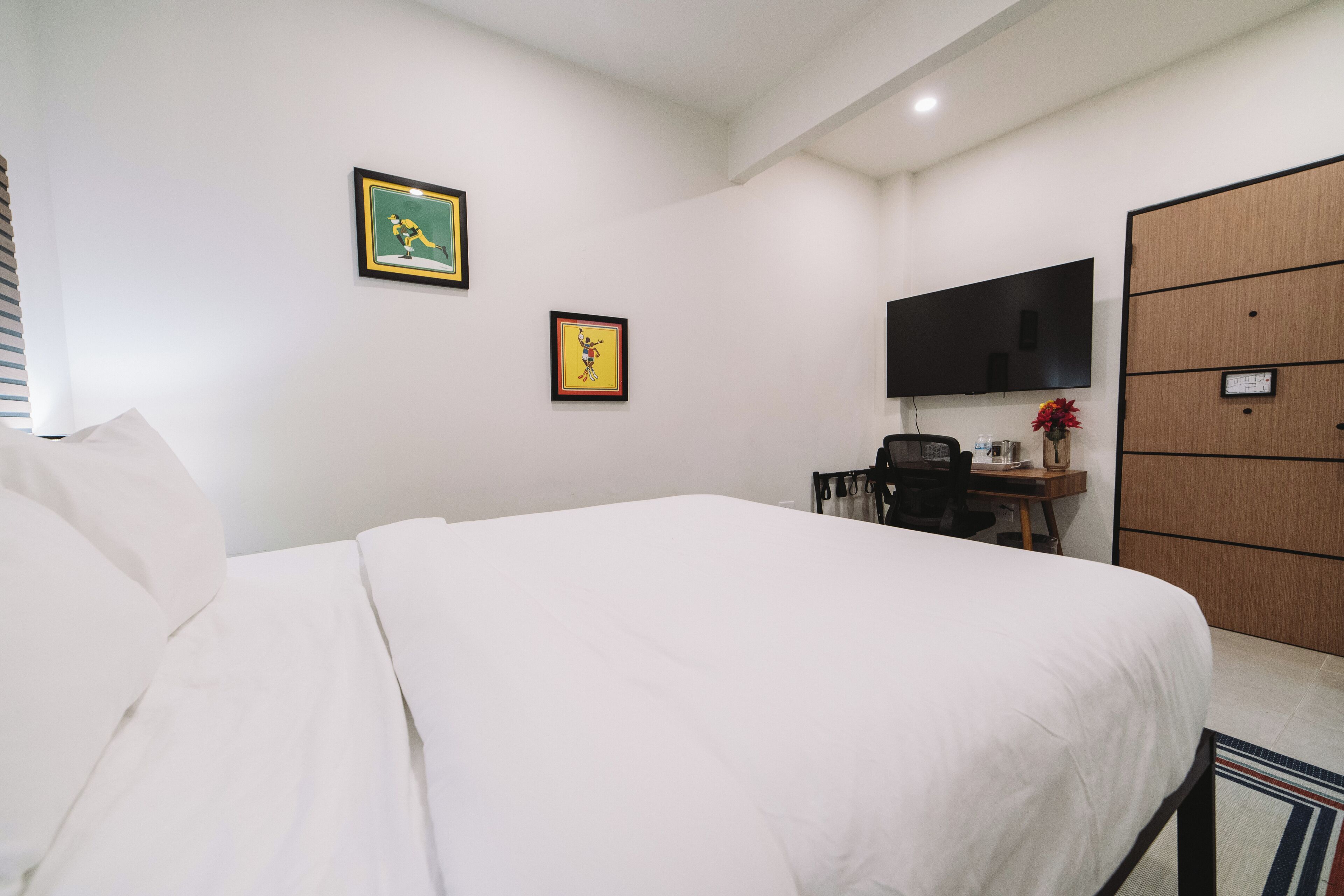 A hotel room with a large bed, a desk with a chair, a flat-screen TV mounted on the wall, and a wooden wardrobe.