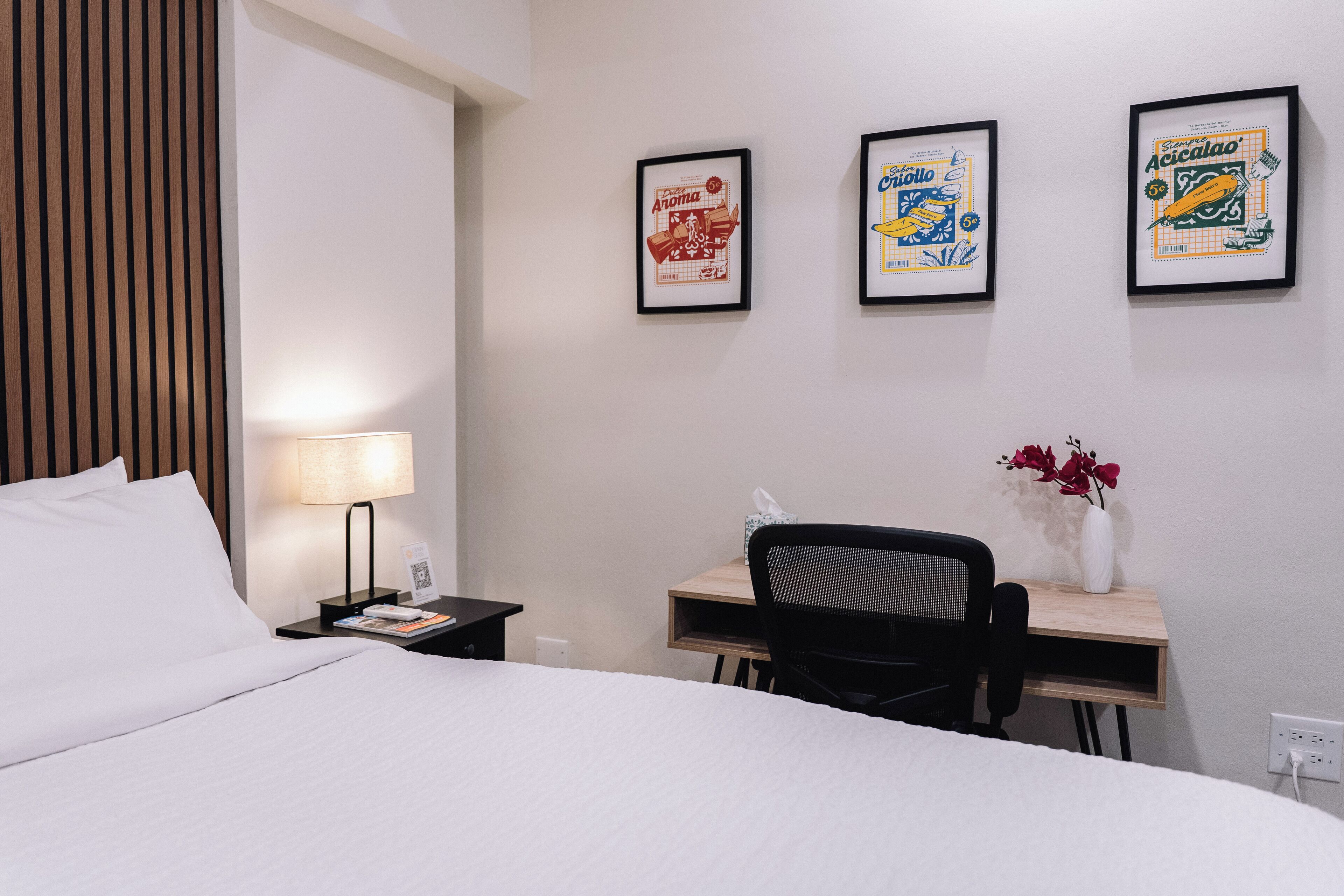 Una camera d'albergo con un letto, una scrivania, una sedia, una lampada e tre quadri appesi alla parete.
