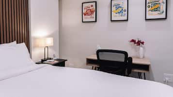 Una camera d'albergo con un letto, una scrivania, una sedia, una lampada e tre quadri appesi alla parete.