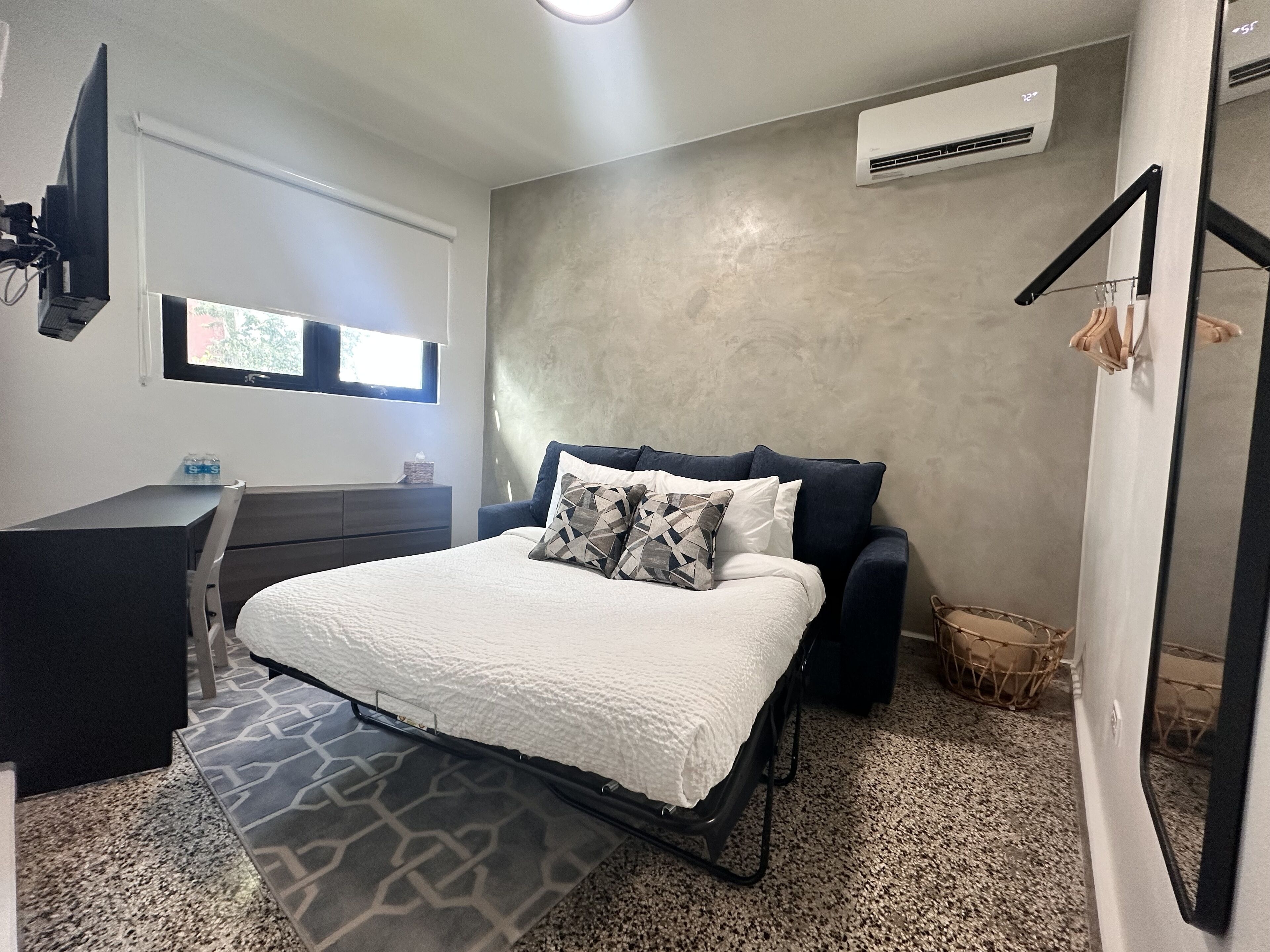 Een slaapkamer met een bed, een dressoir, een televisie en een airconditioner.