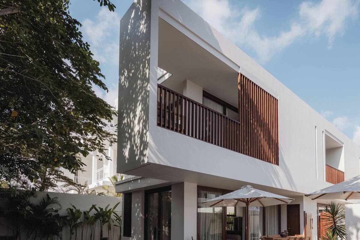 Un moderno edificio de dos pisos con balcón, ventanas amplias y sombrillas exteriores.