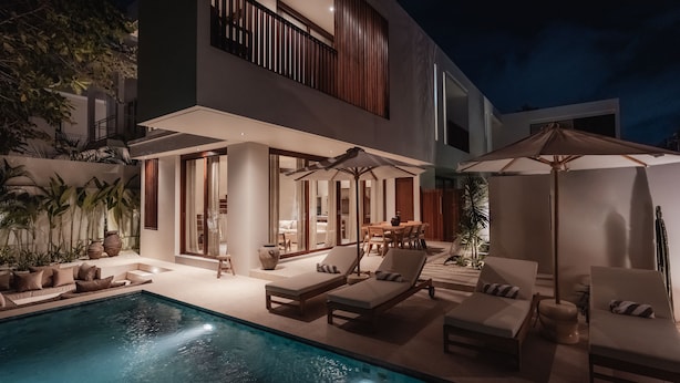 Et moderne hus i to etager med swimmingpool, udendørs møbler og en velbelyst patio.