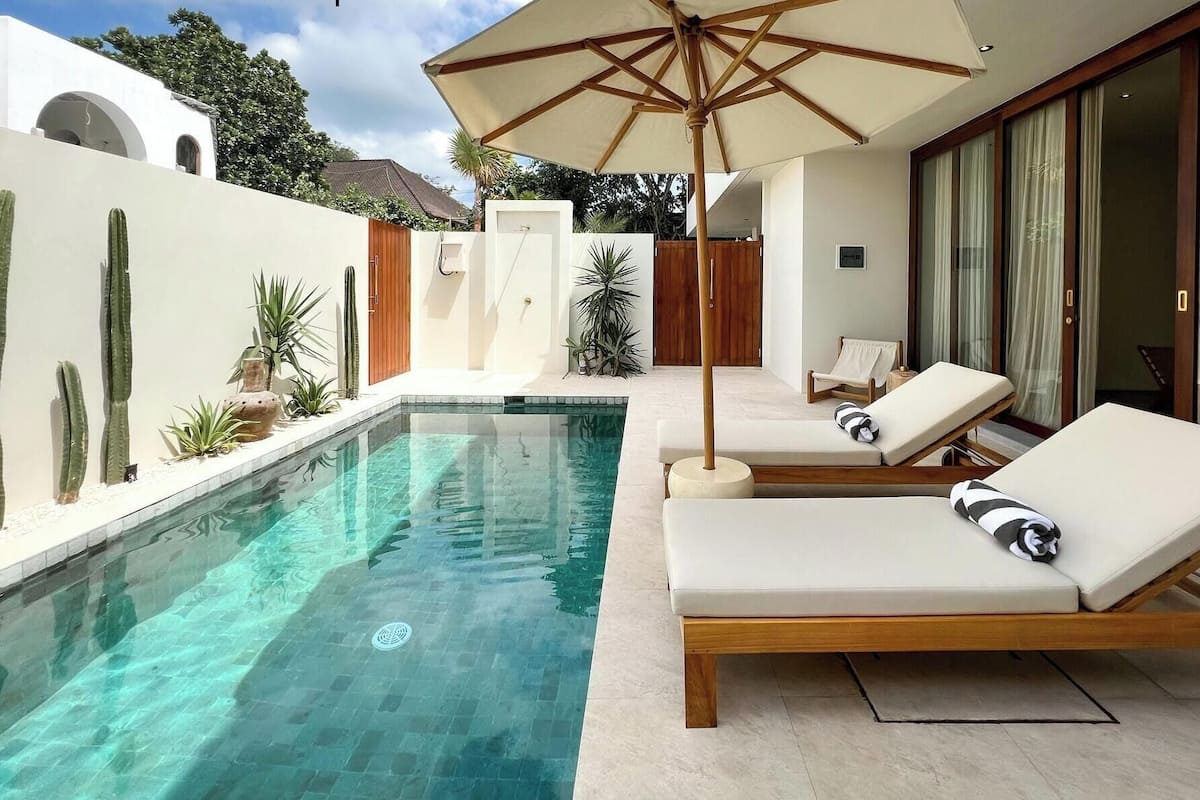 Un área de piscina moderna con agua cristalina, sillas de descanso y una sombrilla grande.