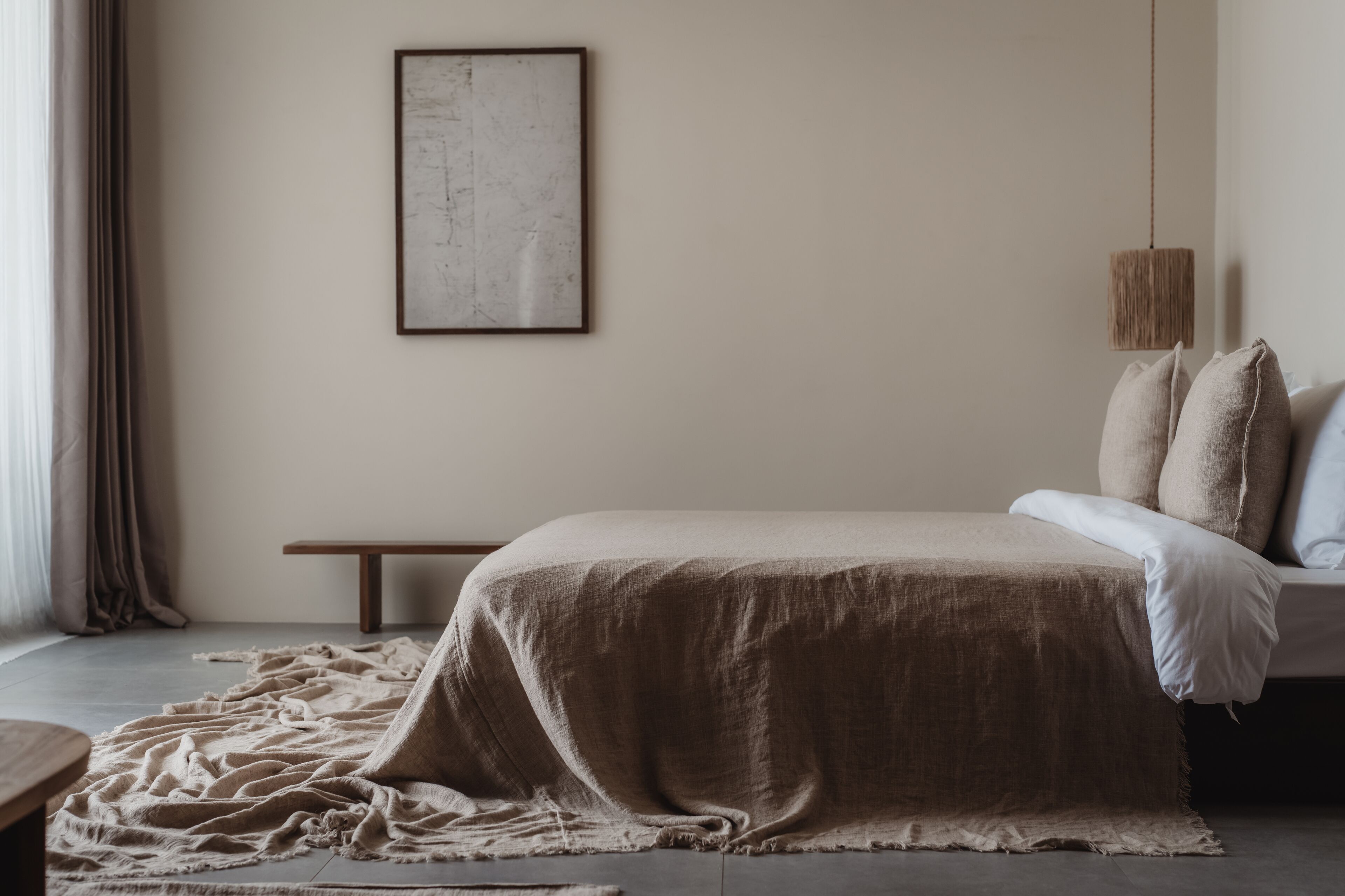 Un dormitorio con cama, un banco, una obra de arte enmarco y una lámpara colgante.