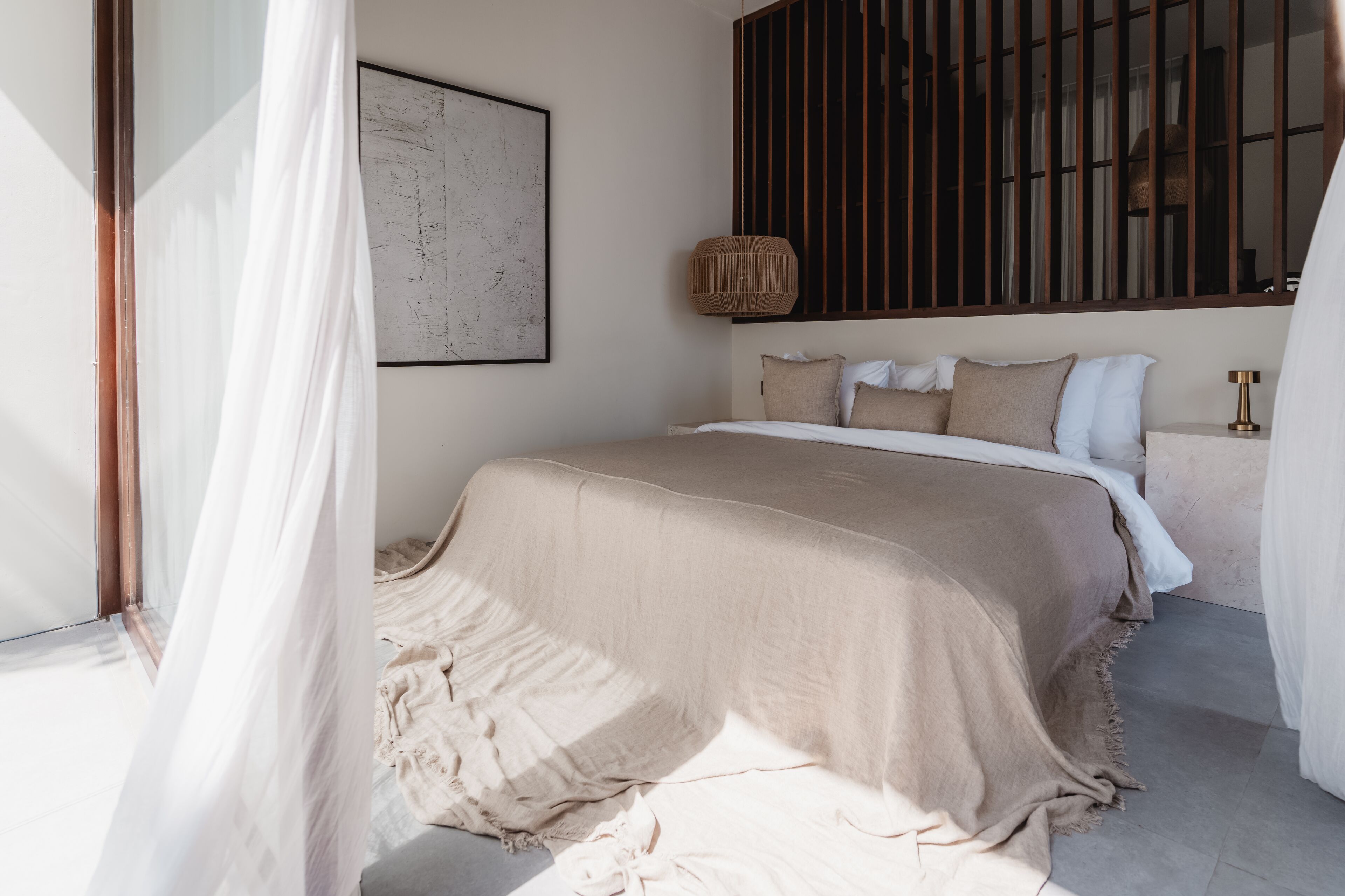 A bedroom with a large bed, a bedside table, a hanging light, and a wall-mounted artwork.