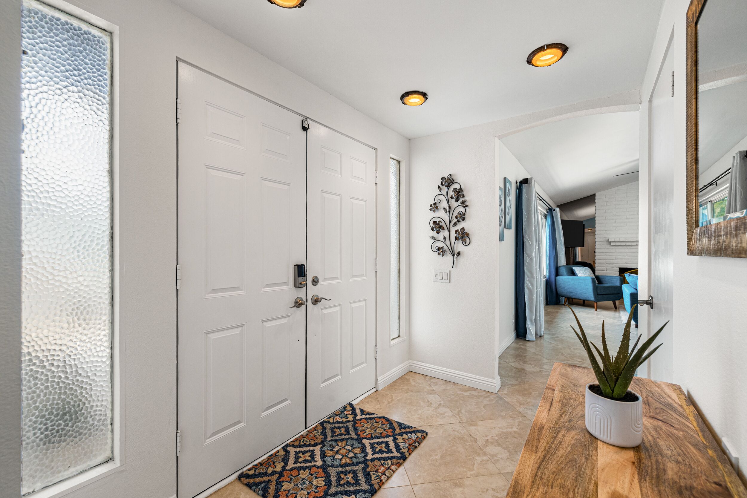 A hallway with double doors, a patterned rug, a potted plant, and a blue couch in the background.