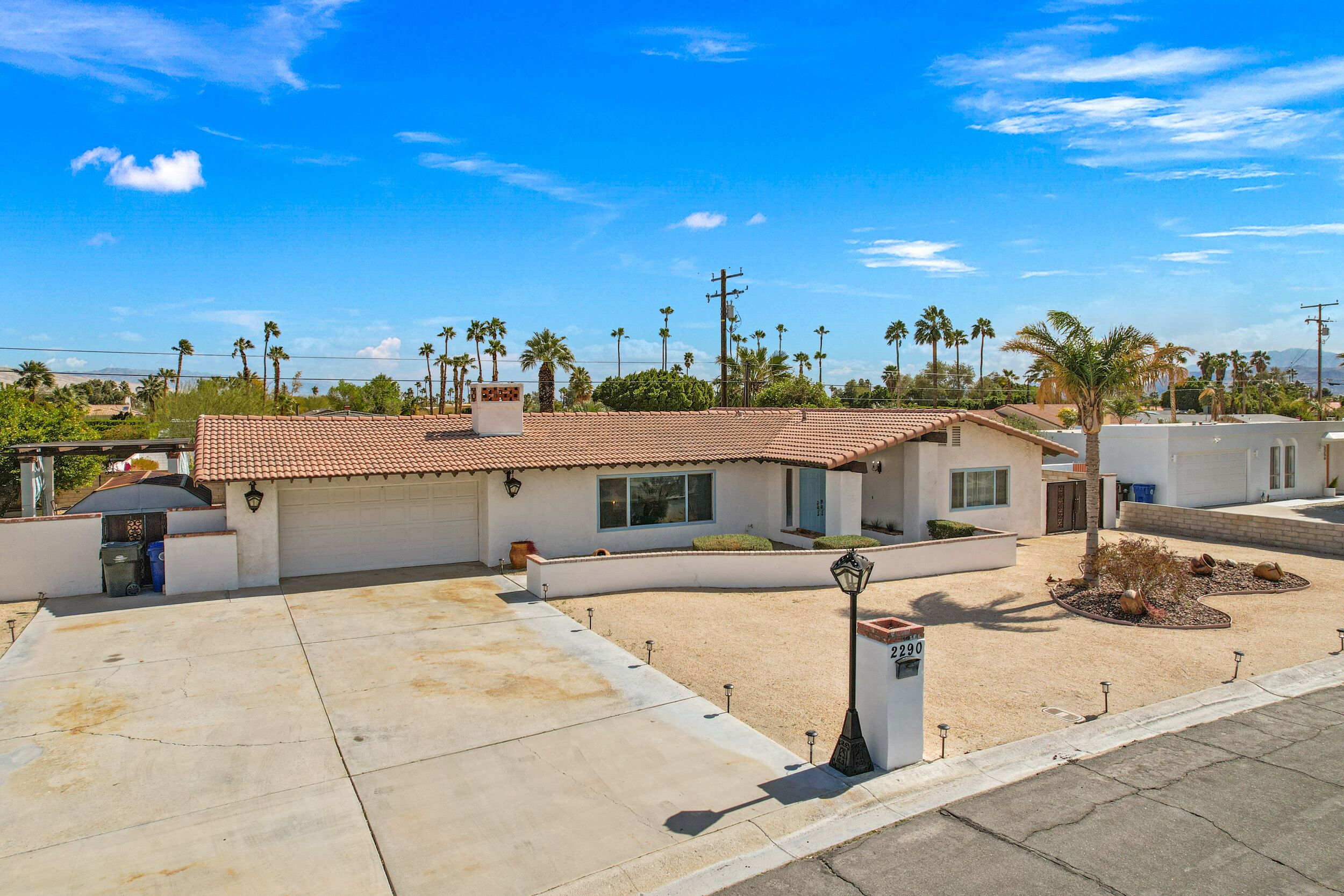A single-story house with a tiled roof, a garage, and a well-maintained lawn with palm trees.