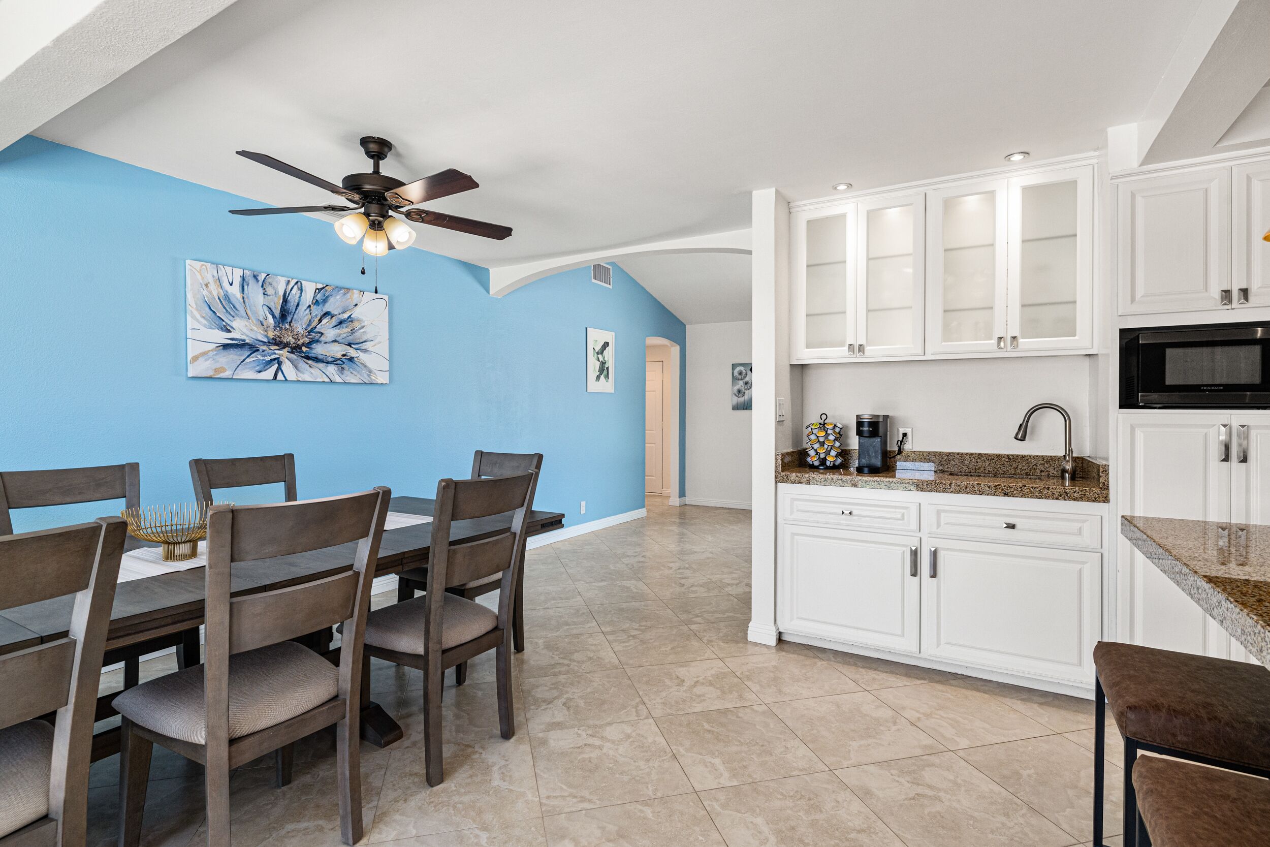 A modern kitchen with white cabinets, a granite countertop, and a ceiling fan.