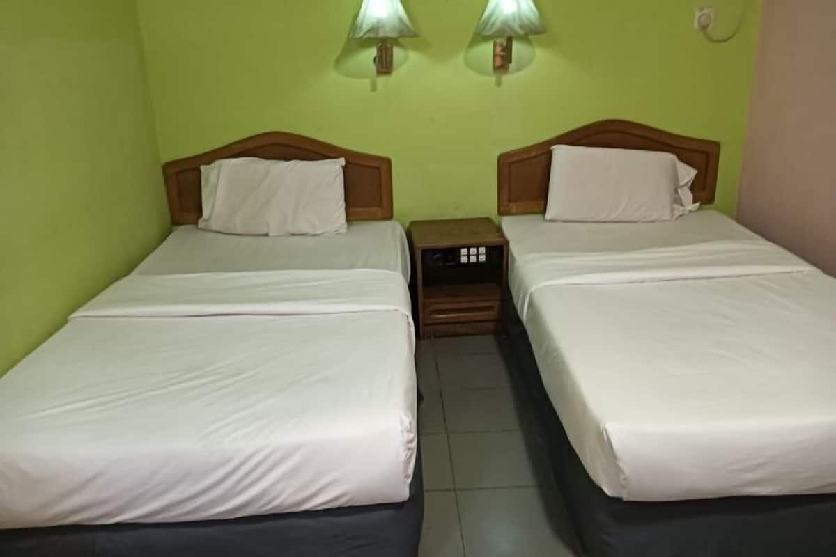 A twin room with two beds, a nightstand, and a wall-mounted lamp between the beds.