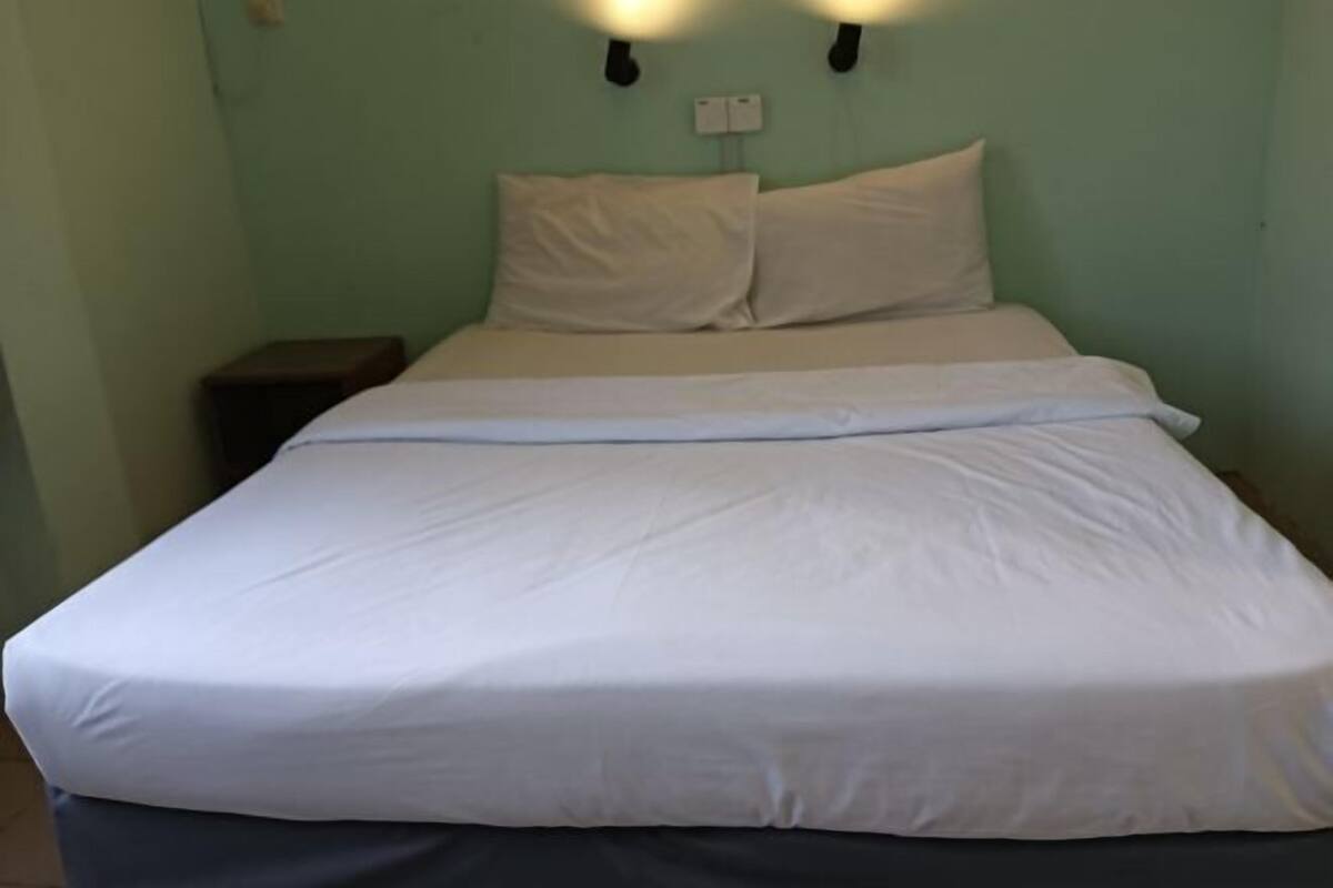 A single bed with white bedding, a nightstand, and a wall-mounted light fixture.