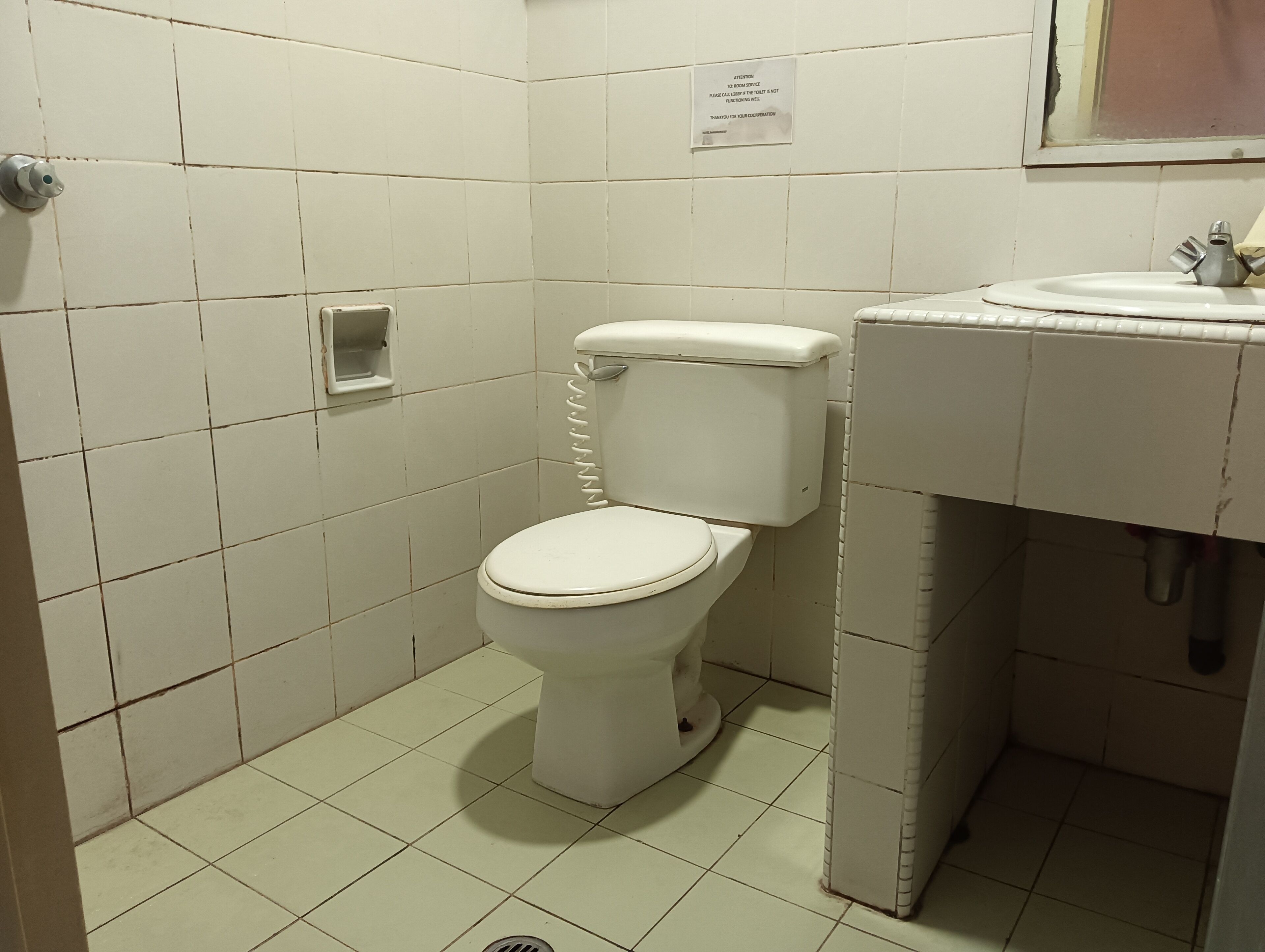 A small, clean bathroom with a toilet, sink, and a notice on the wall.