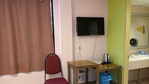 A room with a single red chair, a wooden table with a kettle and a blue basket, a television mounted on the wall, and a bathroom with a sink and mirror. - Hotel O Wawasan Inn (Sarikei)