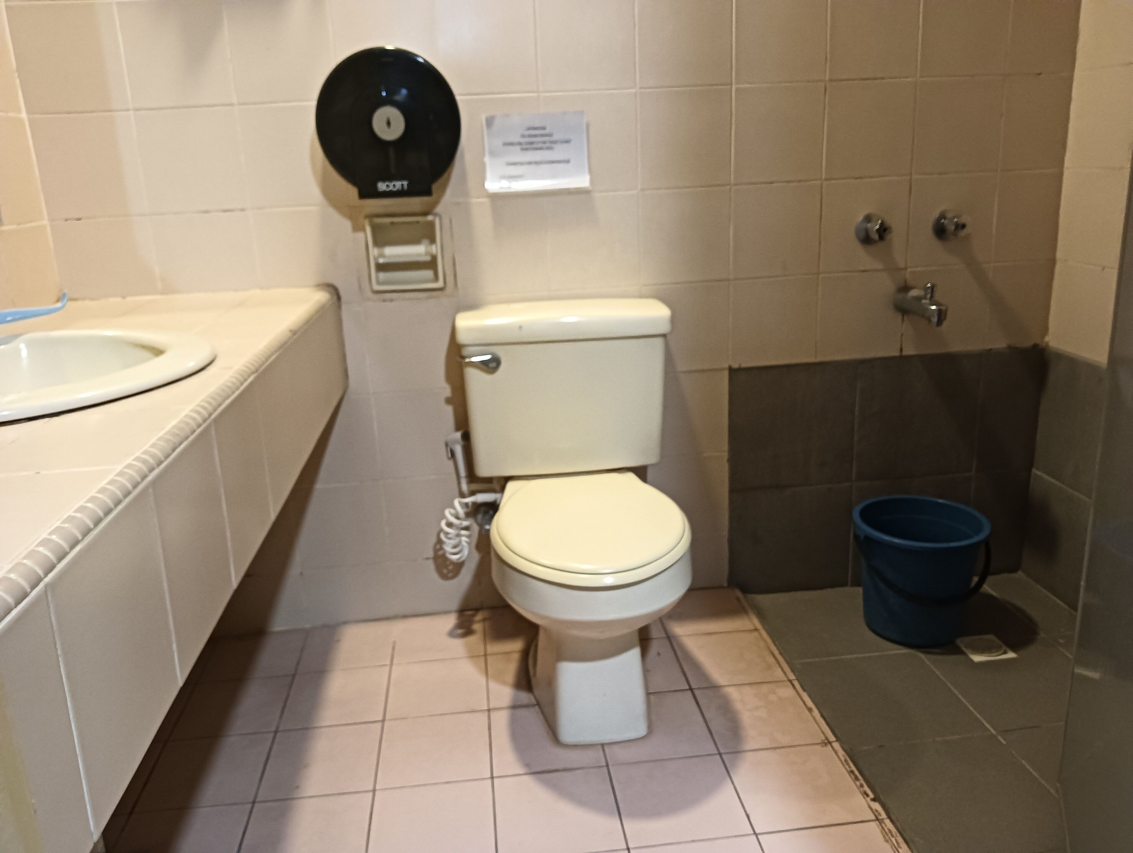 A bathroom with a toilet, a sink, a bidet, and a blue bucket.