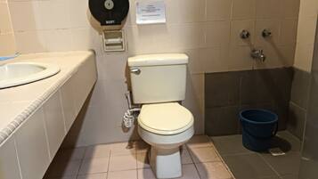 A bathroom with a toilet, a sink, a bidet, and a blue bucket.