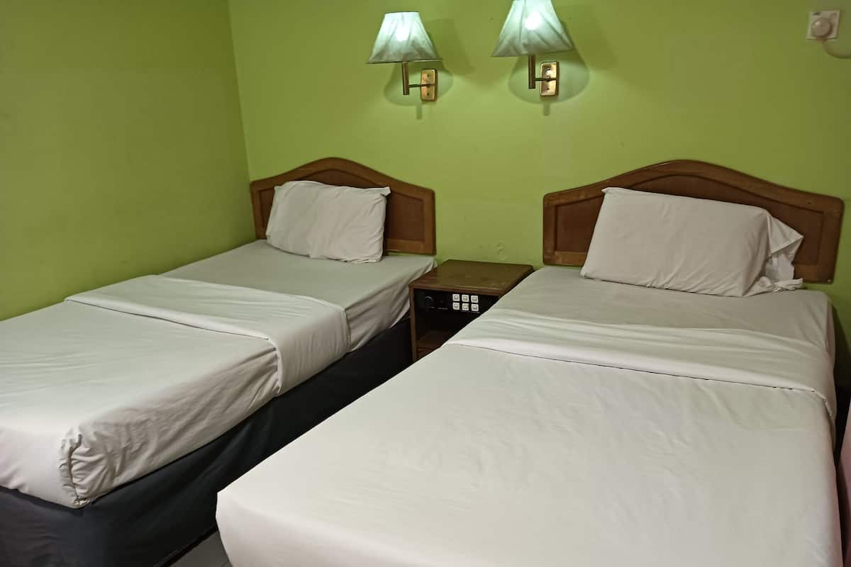 A room with two single beds, each with a wooden headboard and white bedding. There are two wall-mounted lamps and a small table between the beds.